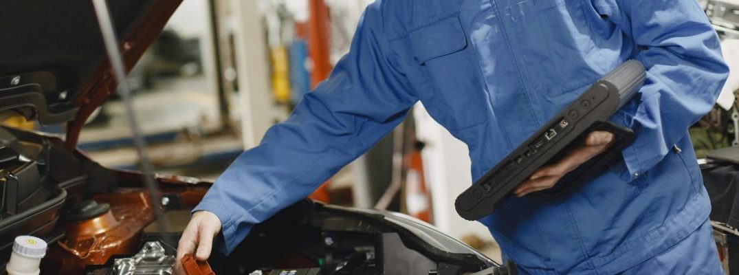 A mechanic works under the hood of a vehicle.
