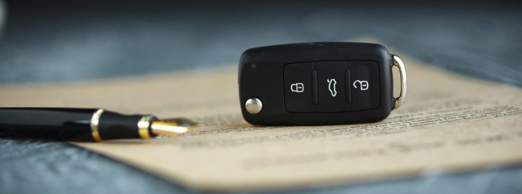 A car key and pen sit on top of the paperwork to buy a used vehicle.