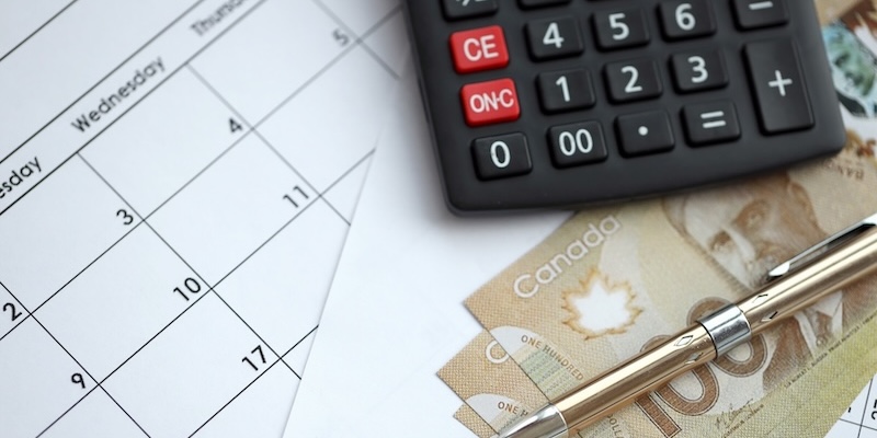 A calculator sits on top of a calendar with Canadian cash and a pen.